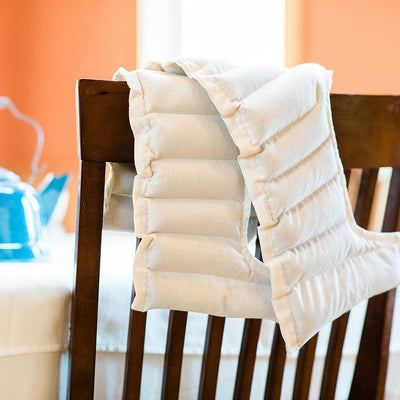 The photo shows a White Parker Mountain deluxe Comfort Wrap hanging off the back of a wooden chair. In the background, there is a blue tea kettle on a white table.