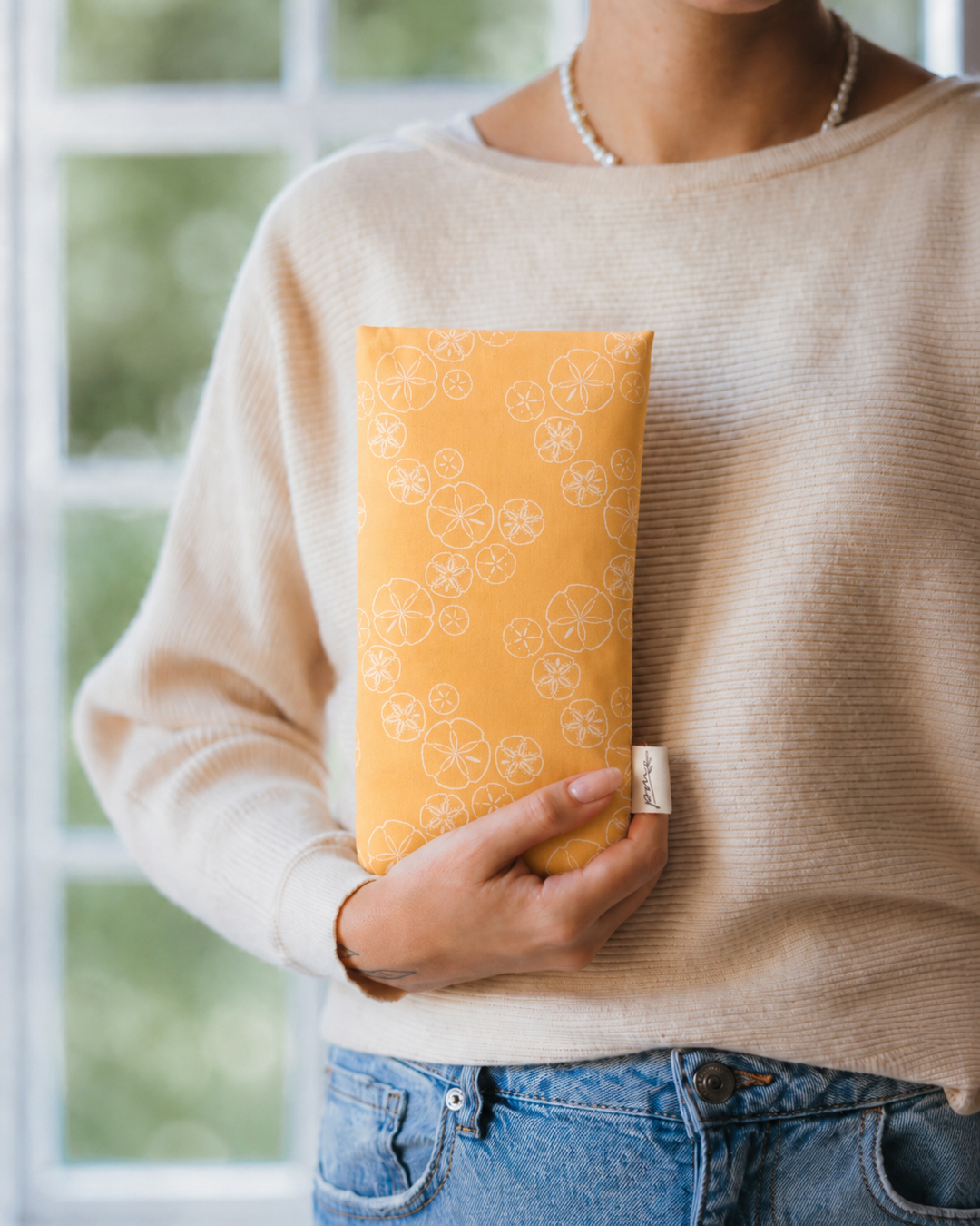 Treasures weighted eye pillow with golden sand dollar print held in hand