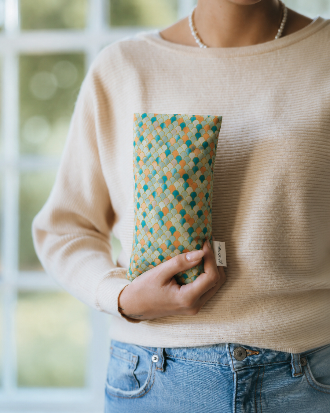 Mermaid weighted eye pillow with teal and coral scale print held in hand
