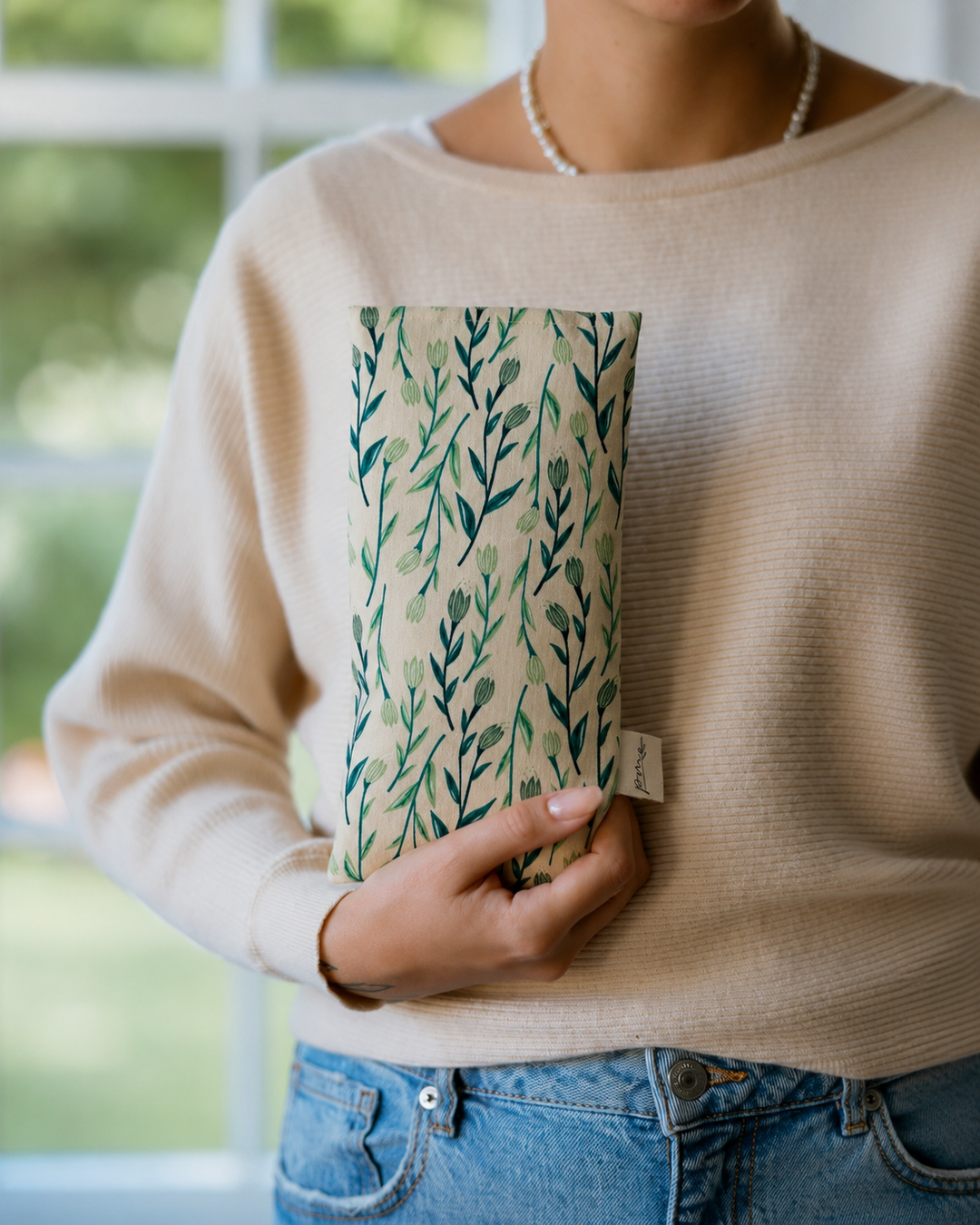 Seagrass weighted eye pillow with green botanical print held in hand