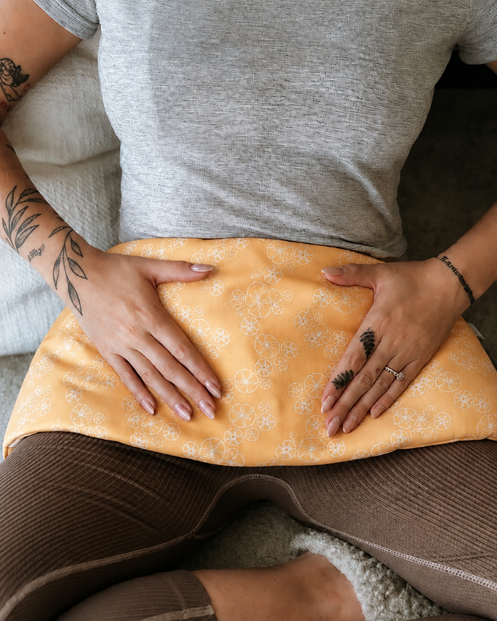 Treasures weighted body wrap with golden sand dollar print resting on lap