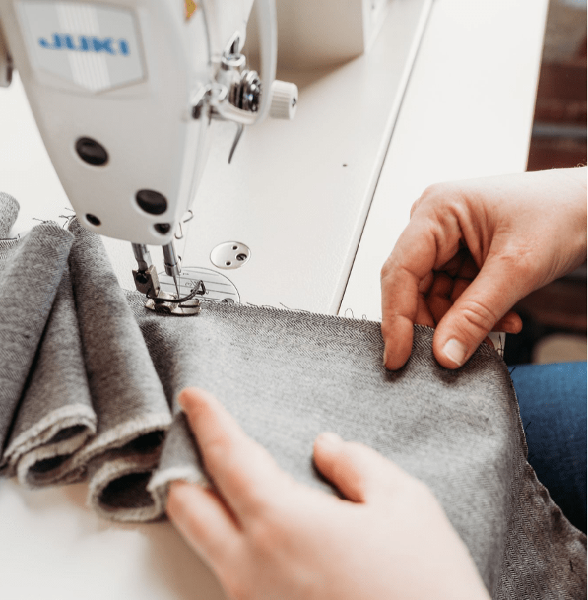 This photo is taken from above showing our employees handcrafting our neck and shoulder weighted comfort wraps. The picture shows two hands using a machine sewing a grey piece of fabric.